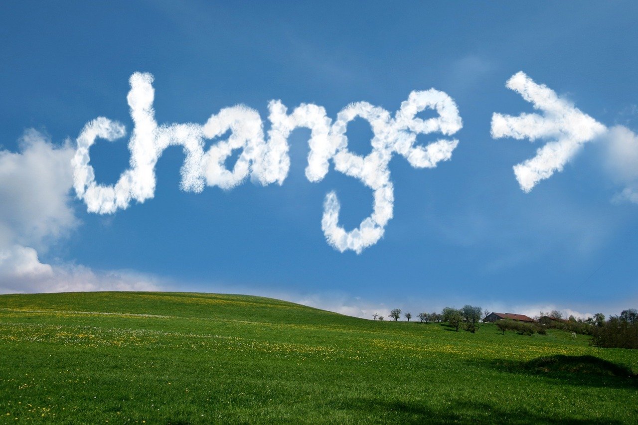 The word 'change' and an arrow formed by clouds in a bright blue sky over a rolling green landscape, symbolizing the transition process in legal software implementation